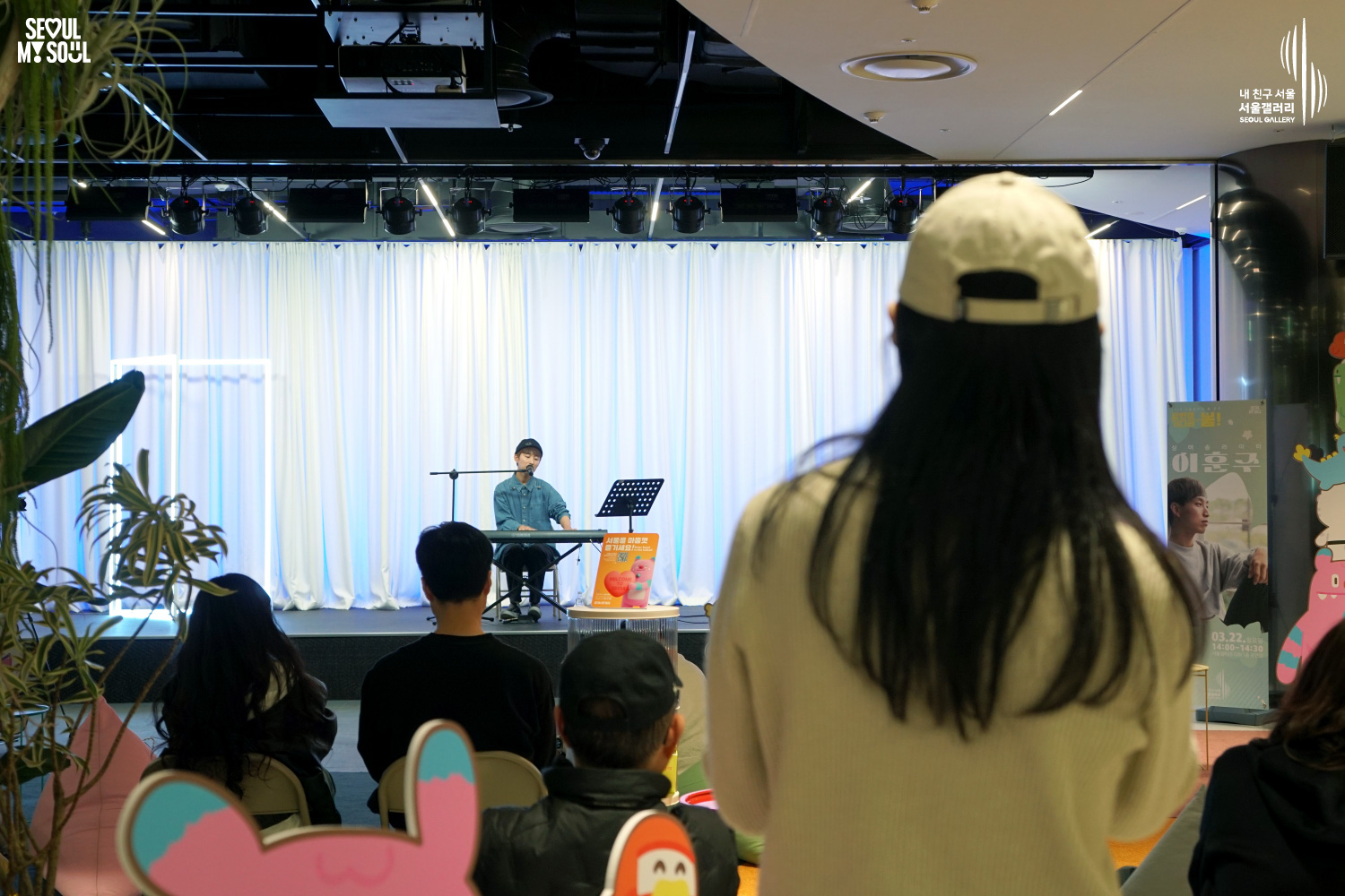 Solo musician Lee Hojun performs vocals and keyboard at Seoul Gallery's Seoul Stage Lounge event before a large seated audience, with "SEOUL MY SOUL" and "Seoul Gallery" logos visible.