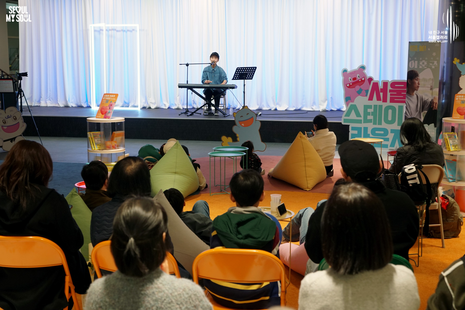 Solo musician Lee Hojun performs vocals and keyboard at Seoul Gallery's Seoul Stage Lounge event before a large seated audience, with "SEOUL MY SOUL" and "Seoul Gallery" logos visible.