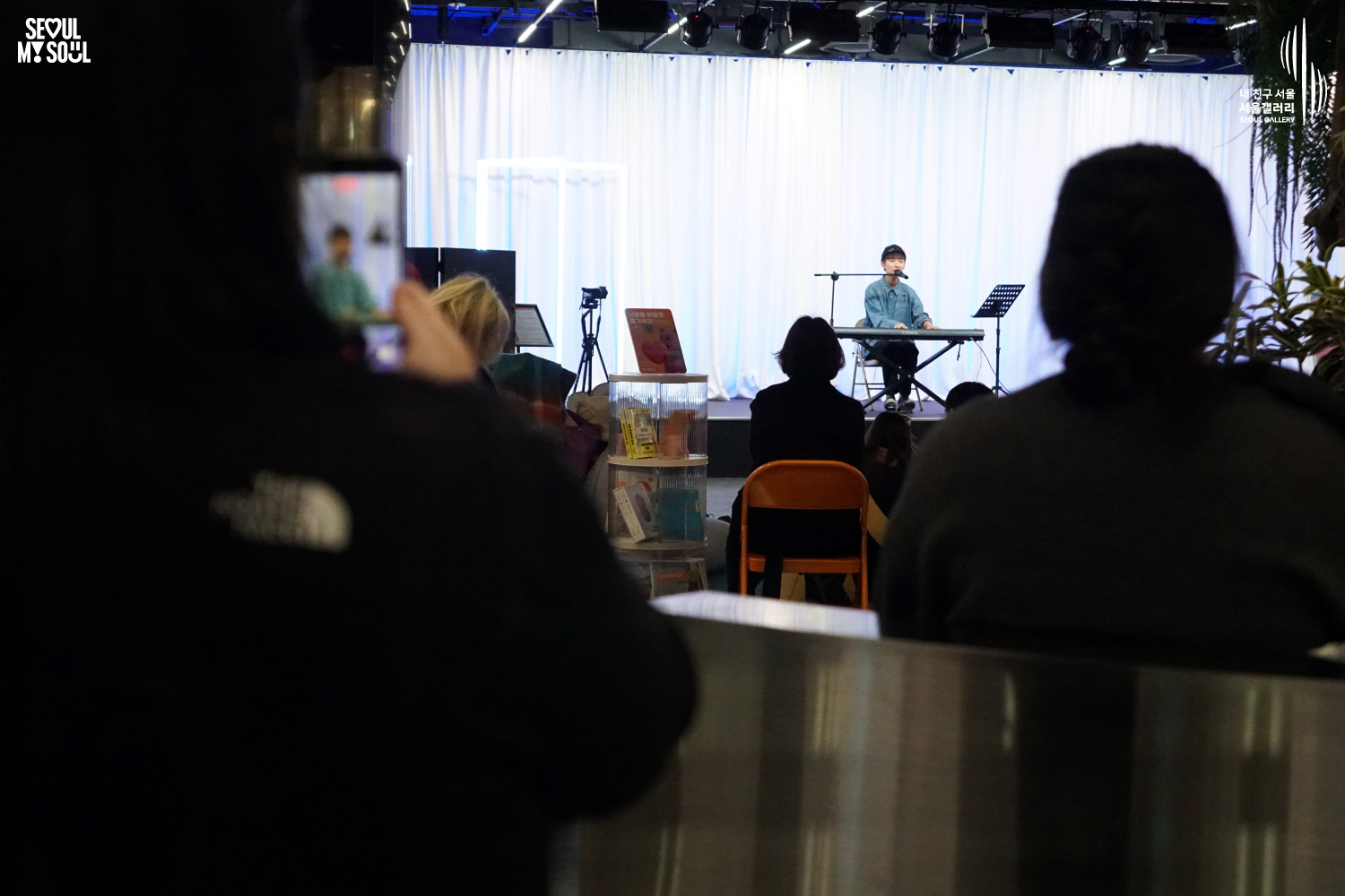 An audience member films a solo keyboardist's performance at Seoul Gallery's Seoul Stage Lounge event, with "SEOUL MY SOUL" and "Seoul Gallery" logos visible.