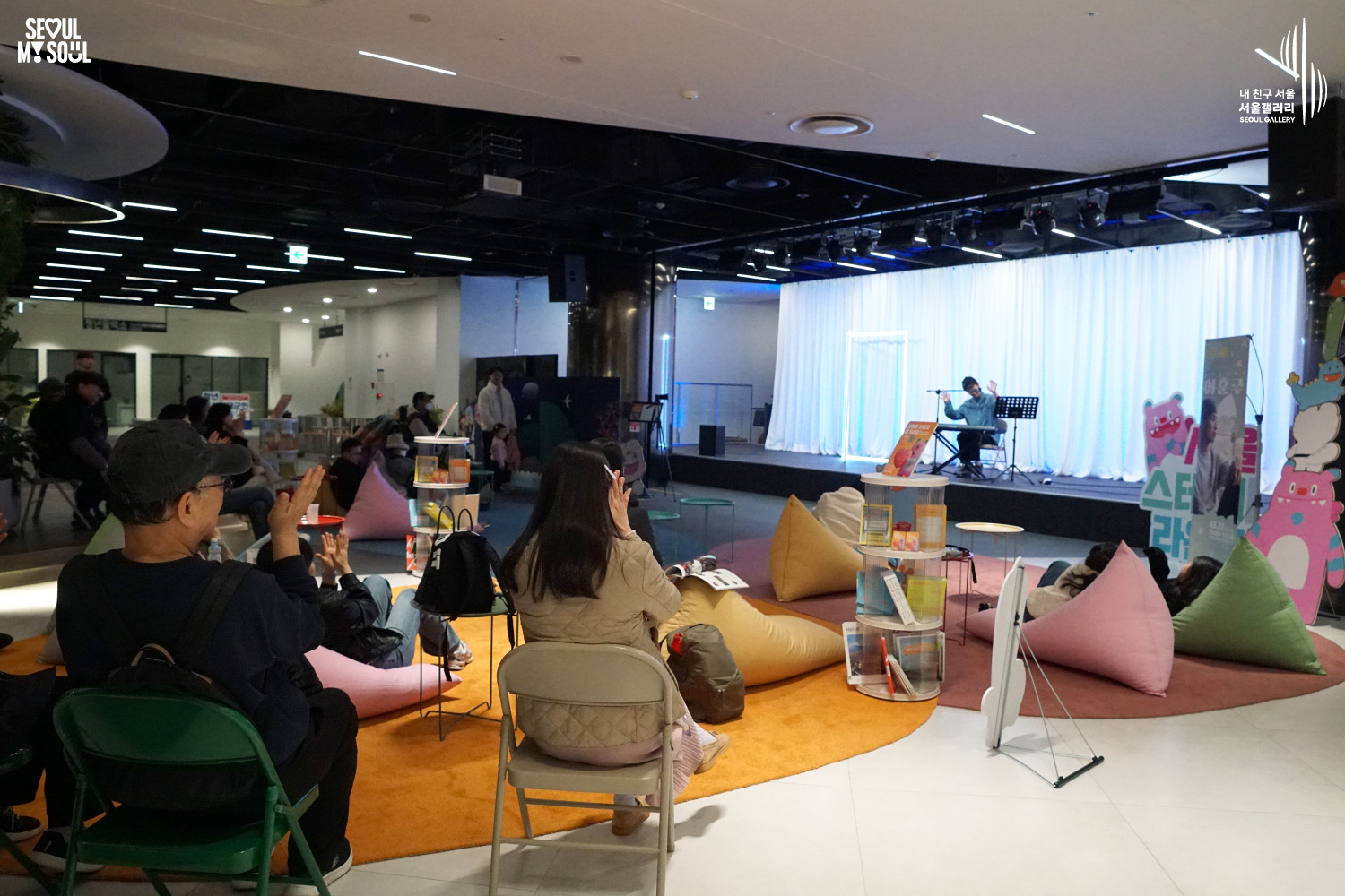 Solo musician Lee Hojun performs vocals and keyboard at Seoul Gallery's Seoul Stage Lounge event before a large seated audience, with "SEOUL MY SOUL" and "Seoul Gallery" logos visible.