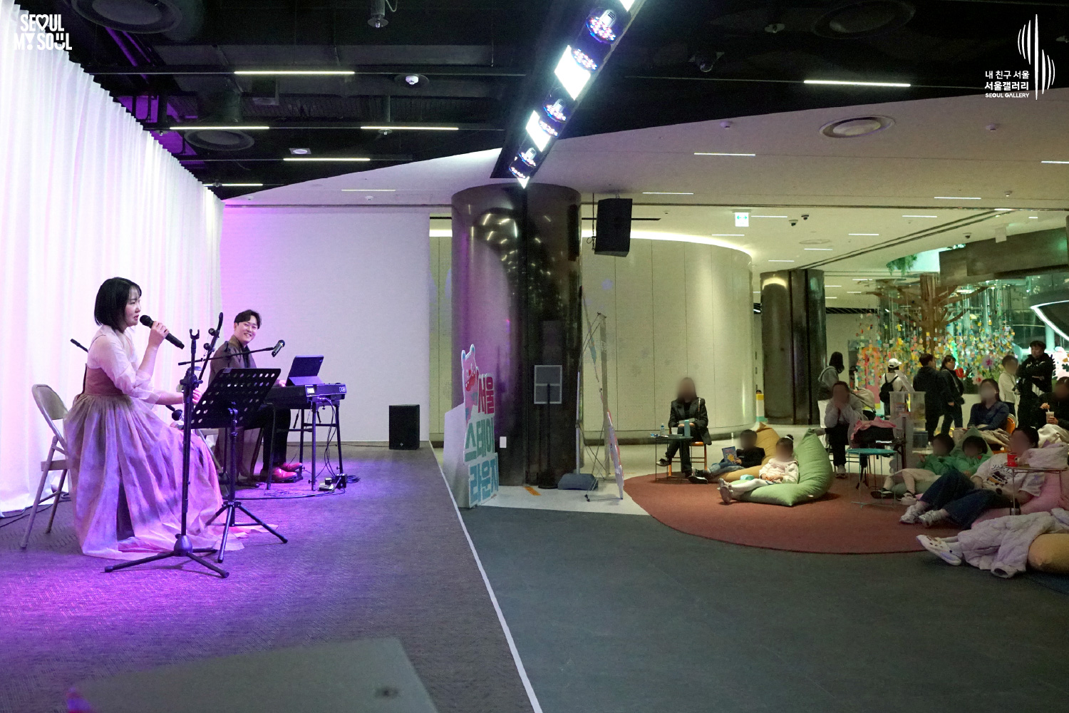 A female vocalist in a pink hanbok and a keyboard player perform at Seoul Gallery's Seoul Stage Lounge event while families relax on beanbag chairs, with "SEOUL MY SOUL" and "Seoul Gallery" logos visible.