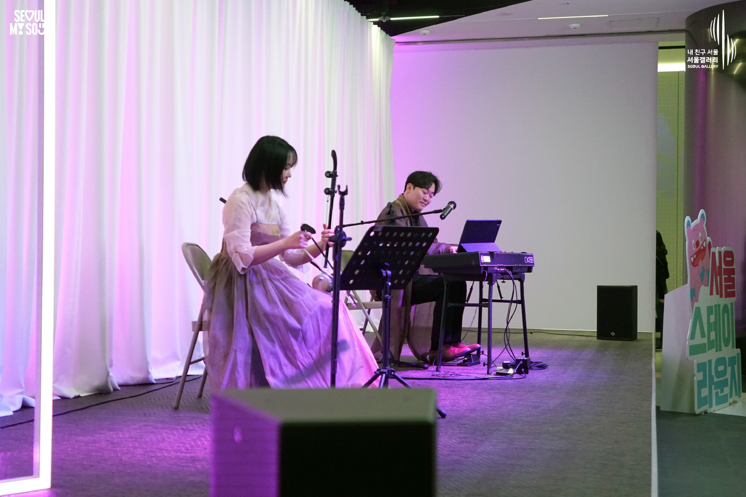 A haegeum player in a hanbok and a keyboard player perform on a purple-lit stage at Seoul Gallery's Seoul Stage Lounge event, with "SEOUL MY SOUL" and "Seoul Gallery" logos visible.