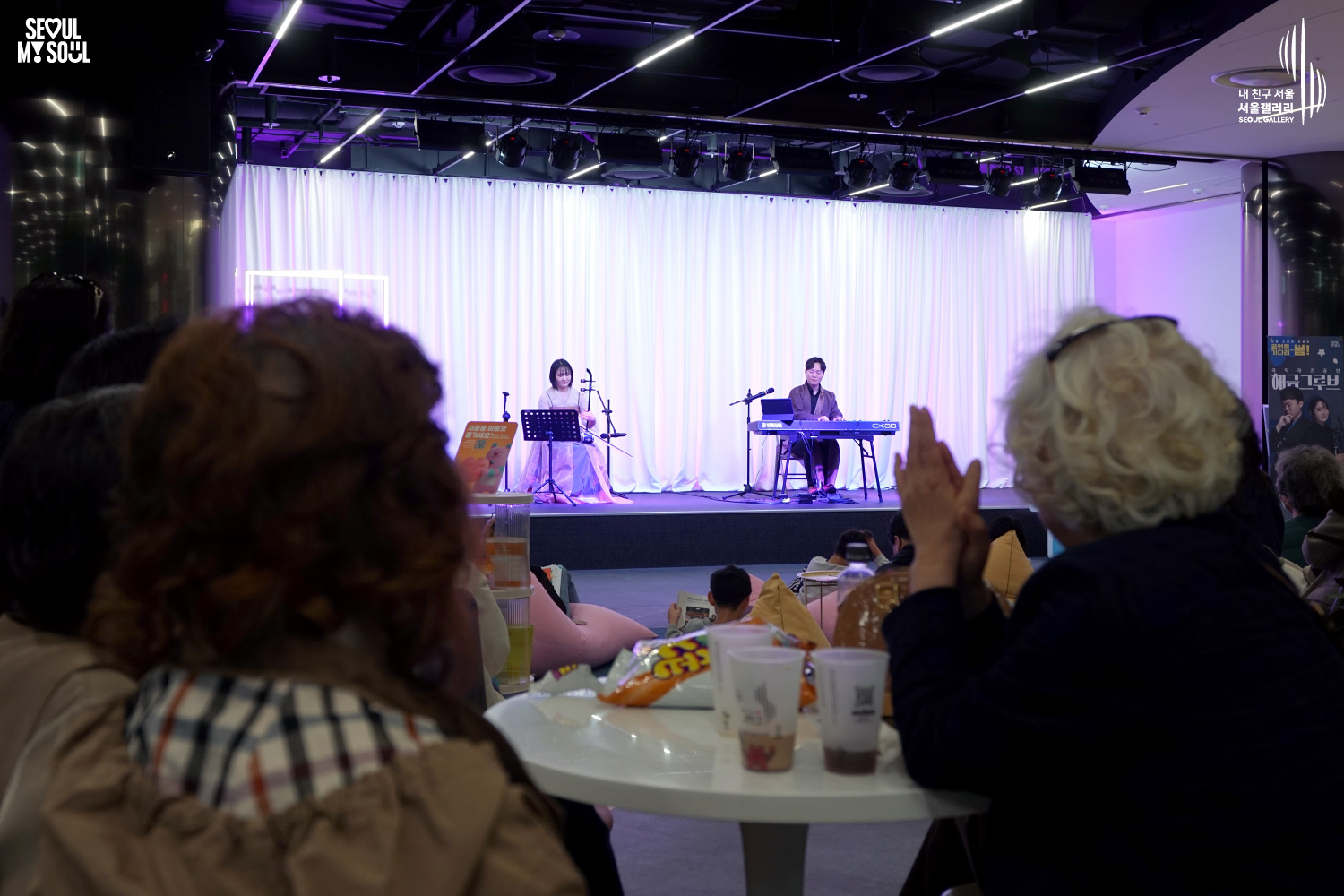 The duo Haegeum Groove (haegeum and keyboard) performs at Seoul Gallery while audience members applaud from cafe-style seating, with "SEOUL MY SOUL" and "Seoul Gallery" logos visible.