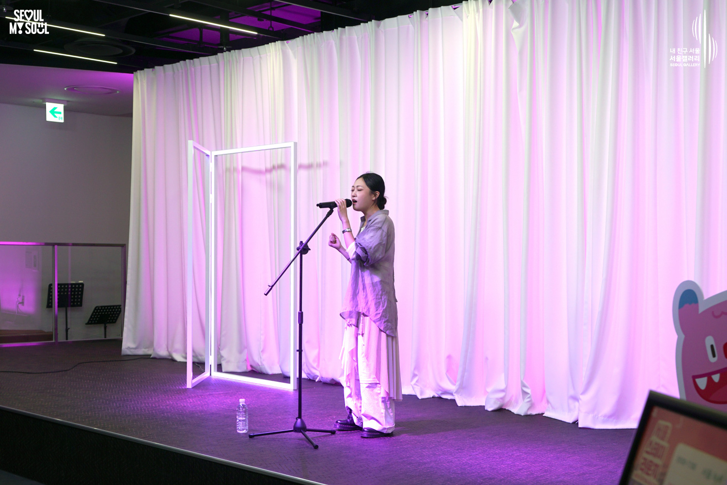 A female vocalist performs solo on a pink-lit stage with white curtains at Seoul Gallery, with "SEOUL MY SOUL" and "Seoul Gallery" logos visible.