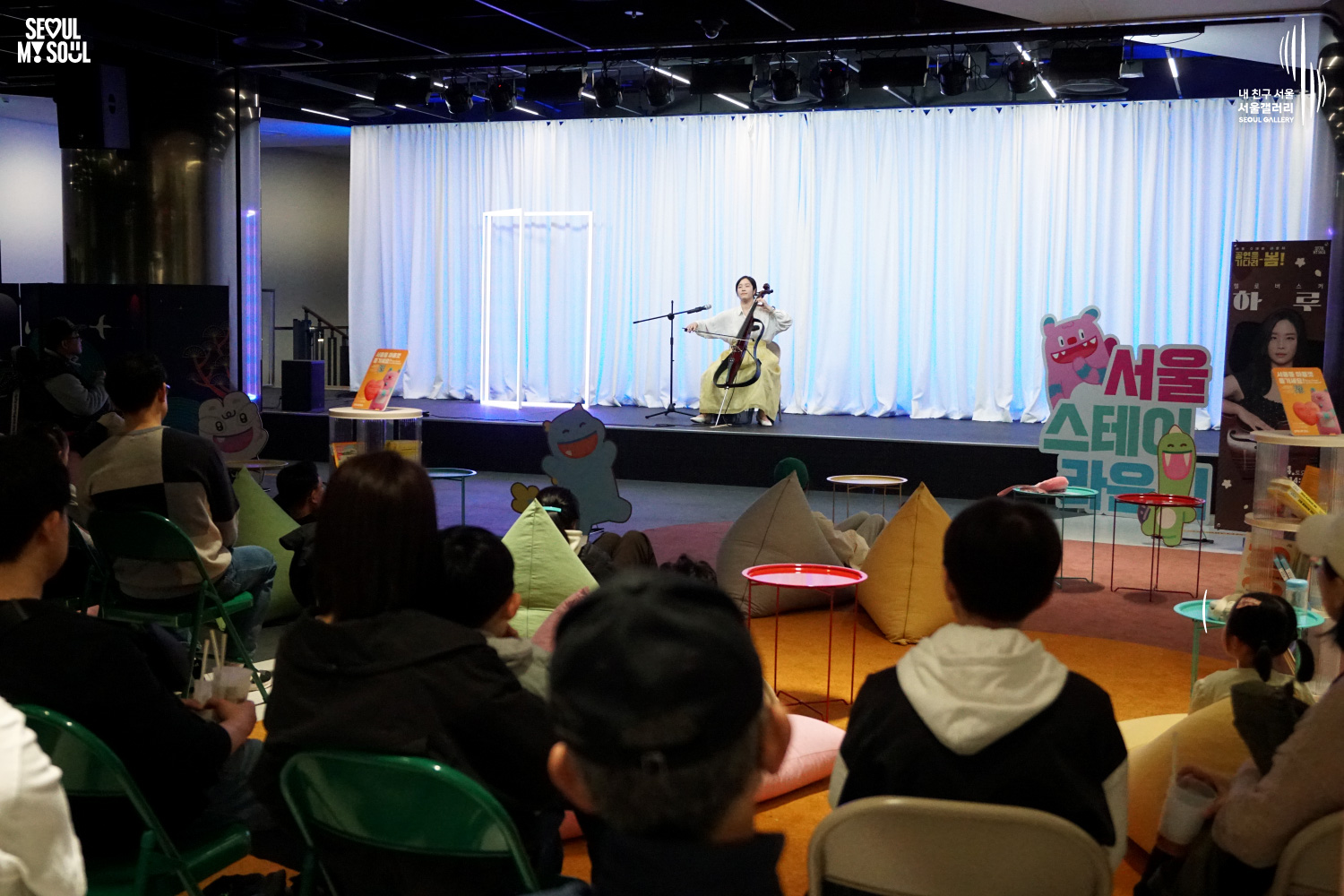 Cellist Haru performs at Seoul Gallery's Seoul Stage Lounge event while audience members watch from beanbags and chairs, with "SEOUL MY SOUL" and "Seoul Gallery" logos visible.