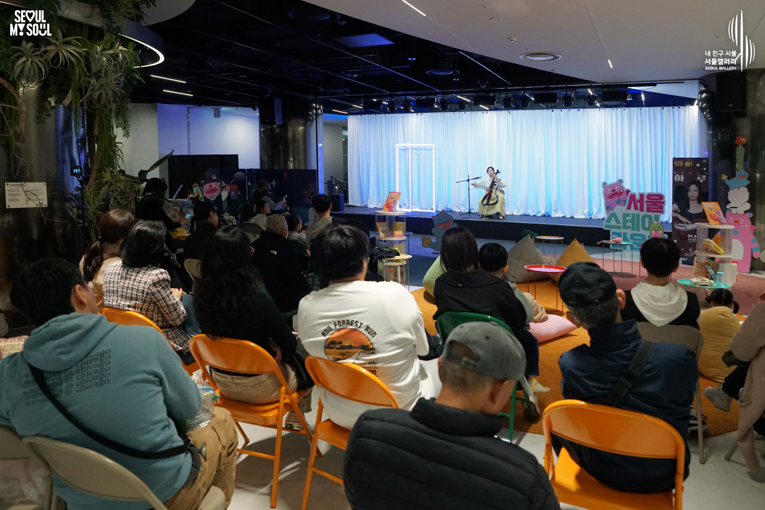 Cellist Haru performs at Seoul Gallery's Seoul Stage Lounge event while audience members watch from beanbags and chairs, with "SEOUL MY SOUL" and "Seoul Gallery" logos visible.