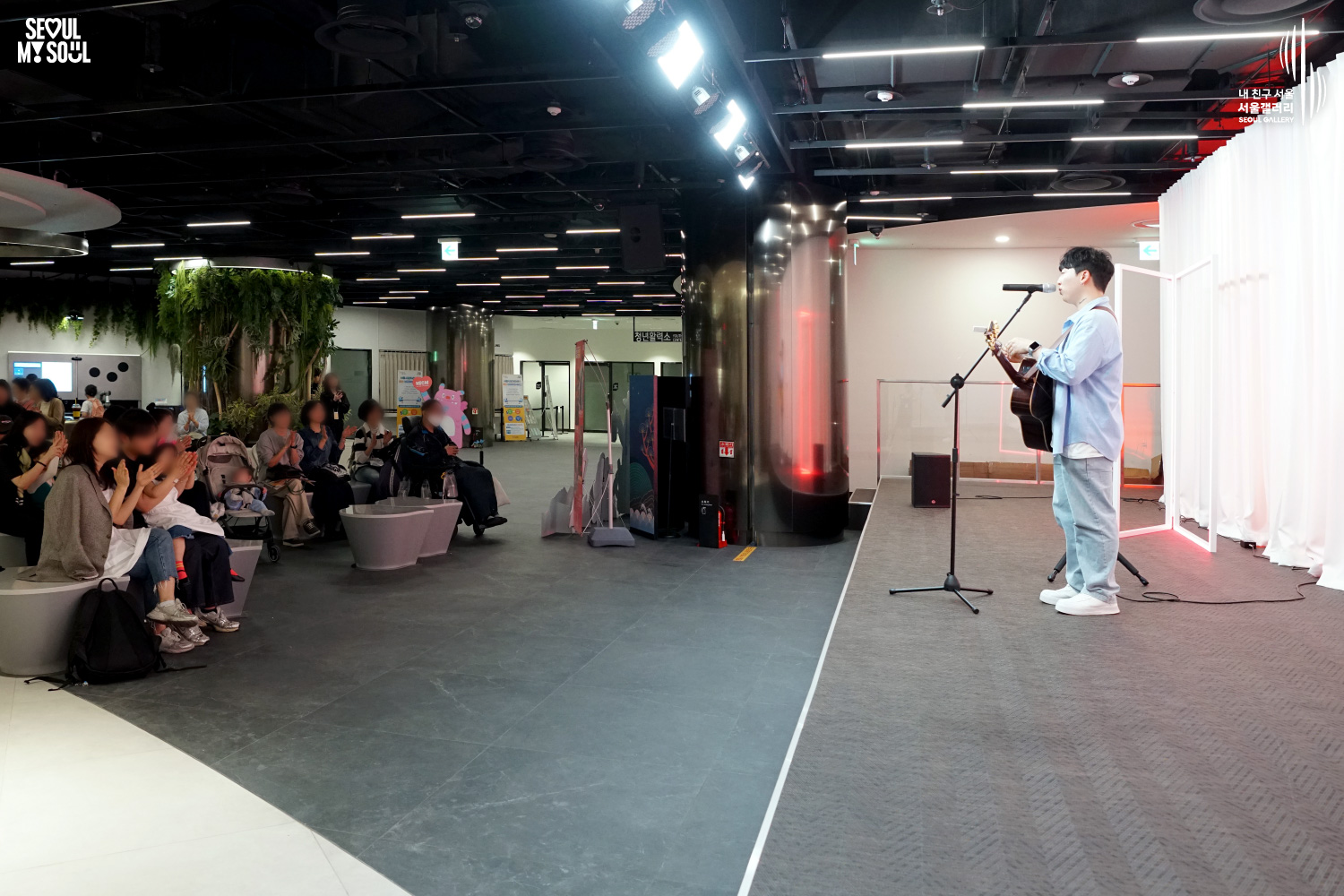 A solo acoustic guitarist performs at Seoul Gallery while audience members including families applaud from the seating area, with "SEOUL MY SOUL" and "Seoul Gallery" logos visible.