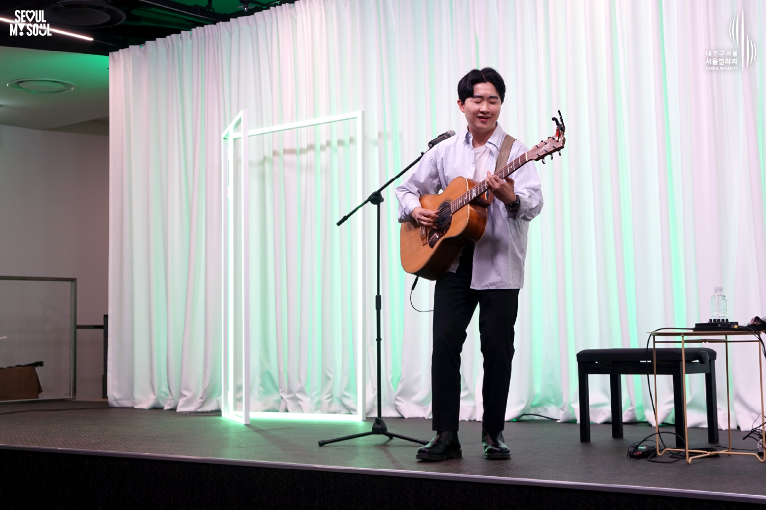 A solo acoustic guitarist sings and plays on a green-lit stage with white curtains at Seoul Gallery, with "SEOUL MY SOUL" and "Seoul Gallery" logos visible.