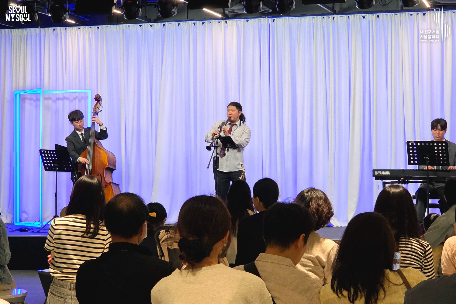 A jazz trio of double bass, clarinet, and keyboard performs on stage at Seoul Gallery before a seated audience, with "SEOUL MY SOUL" and "Seoul Gallery" logos visible.