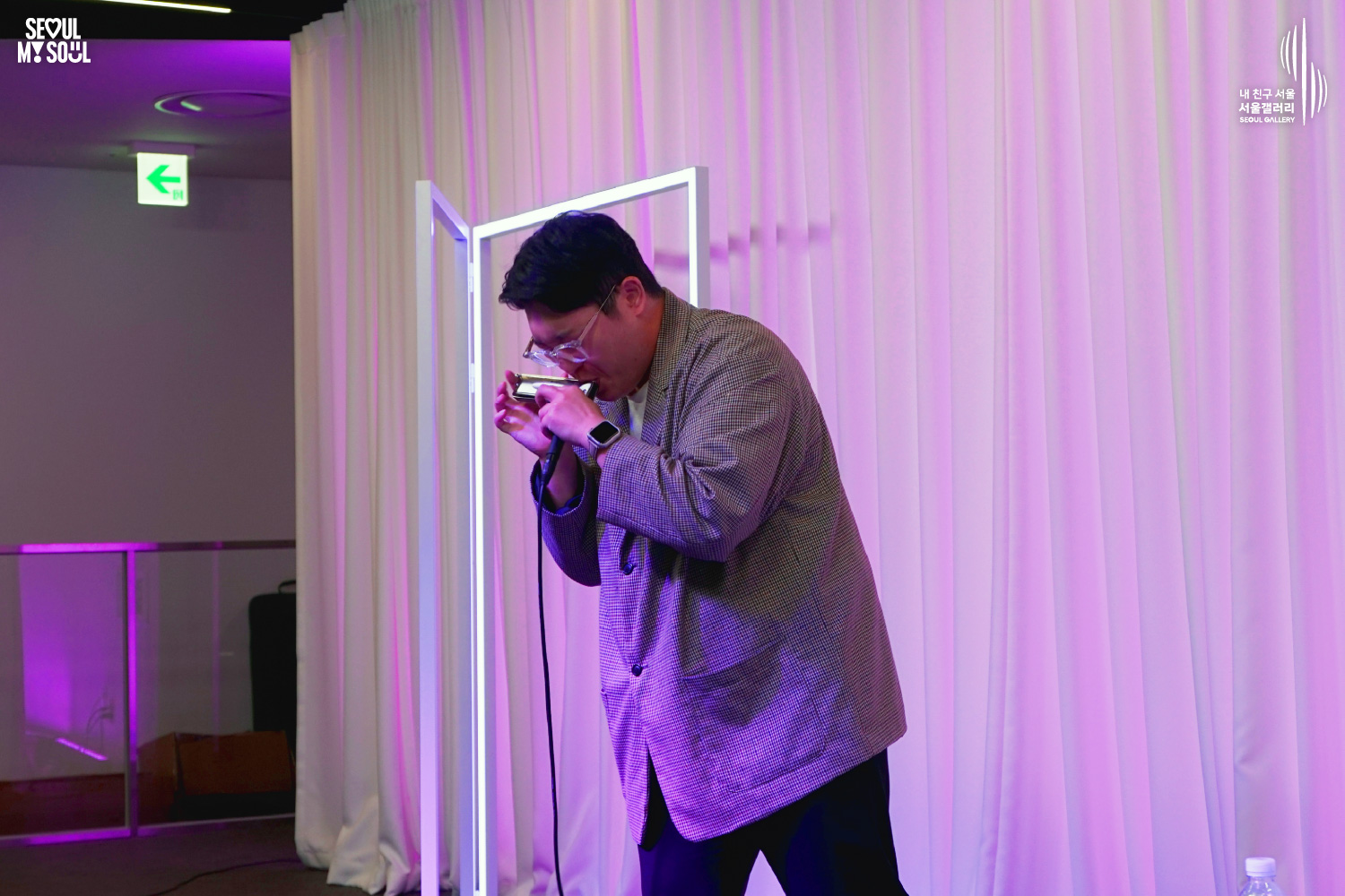 A performer in a checkered jacket plays the harmonica on a purple-lit stage with white curtains at Seoul Gallery, with "SEOUL MY SOUL" and "Seoul Gallery" logos visible.