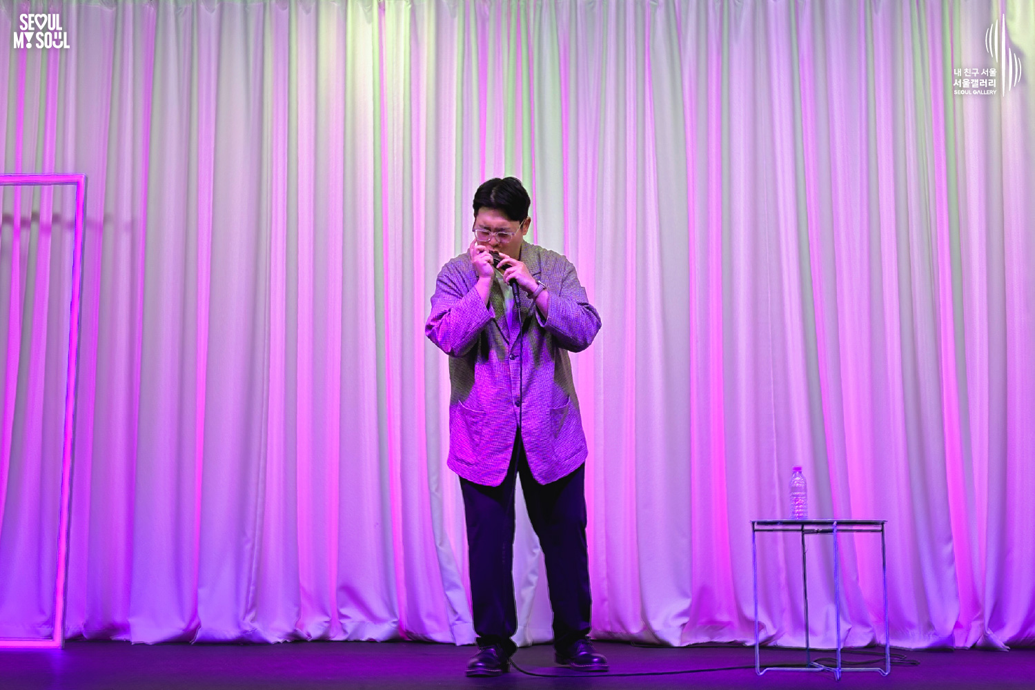 A performer in a checkered jacket plays the harmonica on a purple-lit stage with white curtains at Seoul Gallery, with "SEOUL MY SOUL" and "Seoul Gallery" logos visible.