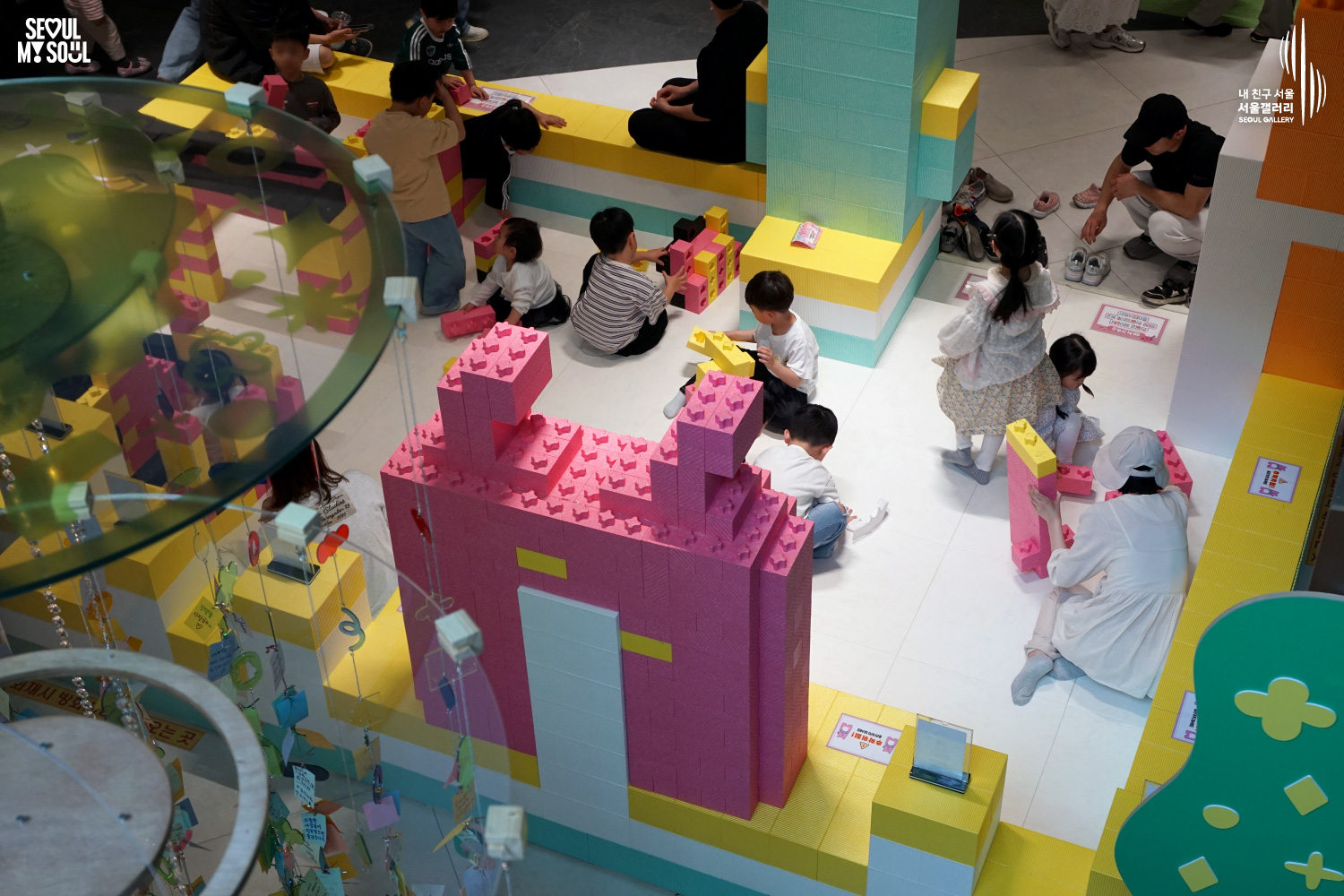 Children play with large foam building blocks in pink, yellow, and teal colors at the Seoul Gallery Kids Lounge, constructing castle-shaped structures together while parents watch nearby.