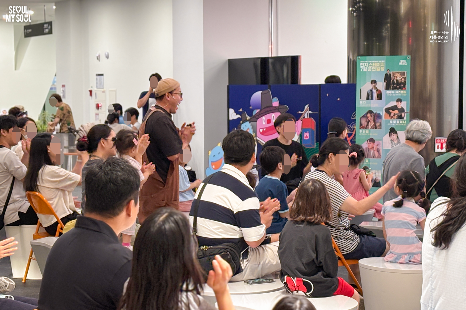 SEOUL MY SOUL 로고와 내 친구 서울 서울갤러리 SEOUL GALLERY 로고가 표기된 서울갤러리 공연장 사진으로, 천장에 무대 조명이 설치된 실내 공간에서 비니 모자와 안경을 착용한 멜빵 의상의 남성 연주자가 객석에서 관람객들과 함께 박수를 치고 있으며, 객석에는 어린이를 포함한 다양한 연령대의 관람객들이 공연을 관람하고 있고 공연 안내판이 함께 보이는 모습이 담긴 이미지입니다.