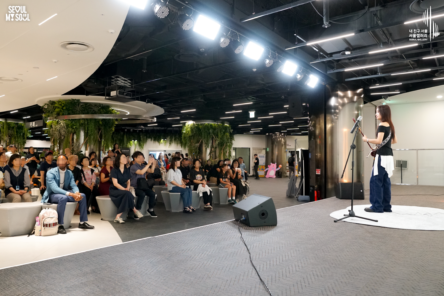 SEOUL MY SOUL 로고와 내 친구 서울 서울갤러리 SEOUL GALLERY 로고가 표기된 서울갤러리 지하 1층 공연장의 공연 현장 사진으로, 천장에 밝은 무대 조명이 설치된 실내 공간에서 긴 머리에 상의와 바지를 입은 여성 연주자가 해금을 들고 마이크 앞에 서 있으며, 무대 앞 객석에는 다양한 연령대의 관람객들이 앉아 공연을 관람하고 일부는 휴대전화로 무대를 촬영하는 모습이 담긴 이미지입니다. 사진 4